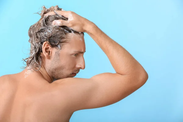 Handsome young man washing hair against color background — Stock Photo, Image