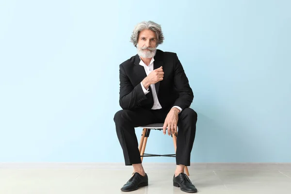 Homem sênior na moda sentado na cadeira perto da parede de cor — Fotografia de Stock