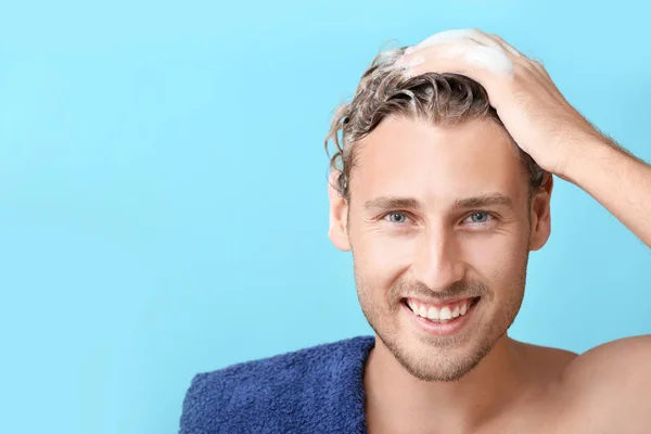Handsome young man washing hair against color background — Stock Photo, Image