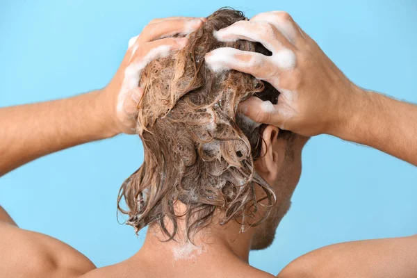 Schöner junger Mann wäscht Haare vor farbigem Hintergrund — Stockfoto