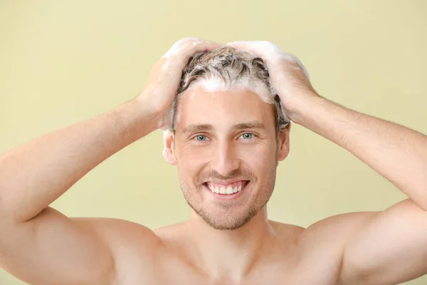 Knappe jonge man die haar tegen kleur achtergrond wast — Stockfoto