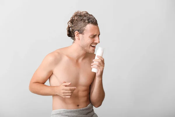 Przystojny młody człowiek za pomocą butelki szamponu jako mikrofon na szarym tle — Zdjęcie stockowe