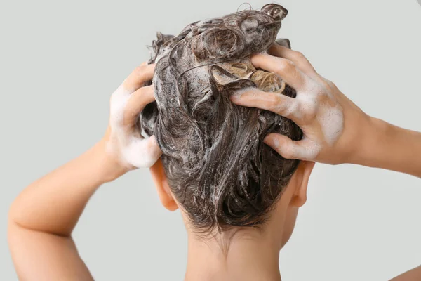 Όμορφη νεαρή γυναίκα πλύσιμο των μαλλιών κατά γκρι φόντο, πίσω όψη — Φωτογραφία Αρχείου