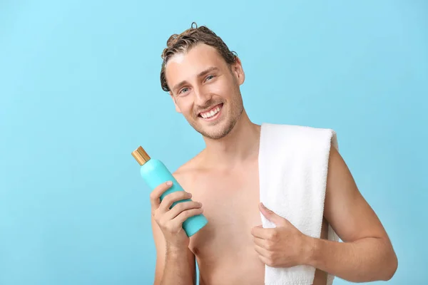 Handsome young man with bottle of shampoo against color background — Stock Photo, Image