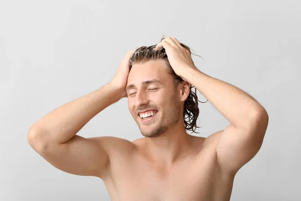 Handsome young man washing hair against grey background