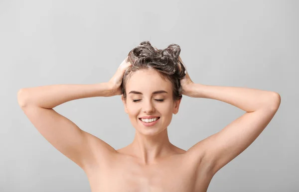 Mulher bonita lavando o cabelo contra fundo cinza — Fotografia de Stock