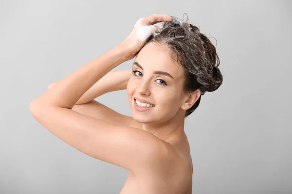 Mulher bonita lavando o cabelo contra fundo cinza — Fotografia de Stock