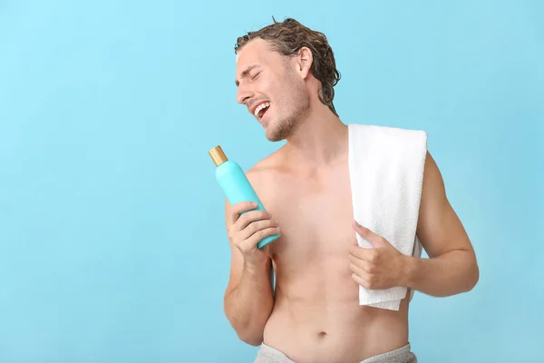 Красивий молодий чоловік використовує пляшку шампуню як мікрофон на кольоровому фоні — стокове фото