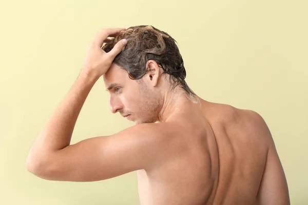 Handsome young man washing hair against color background