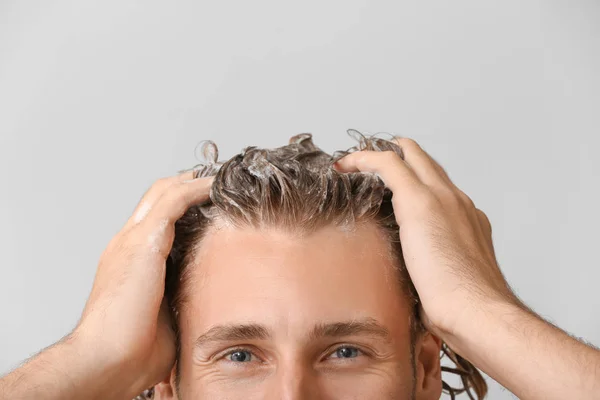 Schöner junger Mann wäscht Haare vor grauem Hintergrund — Stockfoto