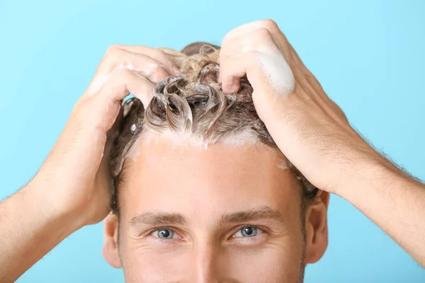 Handsome young man washing hair against color background, closeup