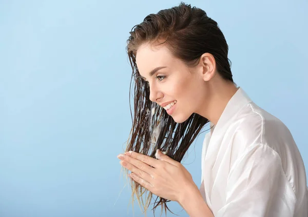 Beautiful young woman applying mousse on her hair after washing against color background — Stock Photo, Image