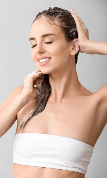 Hermosa joven lavando el cabello contra fondo gris — Foto de Stock