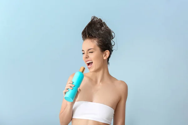 Beautiful young woman using bottle of shampoo as microphone against color background — Stock Photo, Image