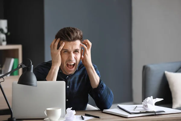 Stressed young man at table in office — Stock Photo, Image