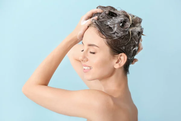 Mooie jonge vrouw die haar tegen kleur achtergrond wast — Stockfoto