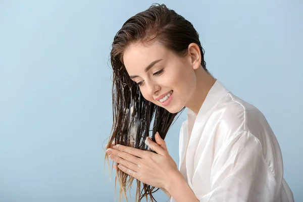 Beautiful young woman applying mousse on her hair after washing against color background — Stock Photo, Image