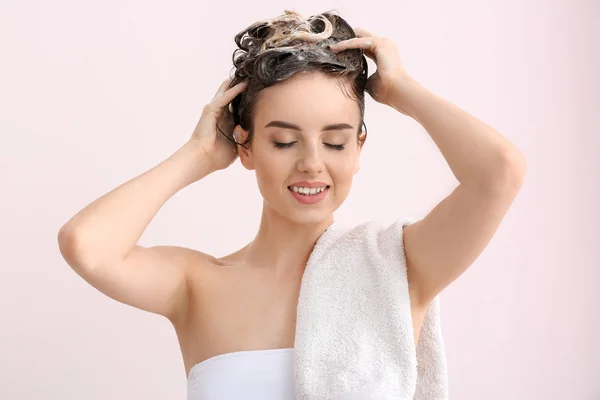 Bella giovane donna lavare i capelli contro sfondo di colore chiaro — Foto Stock