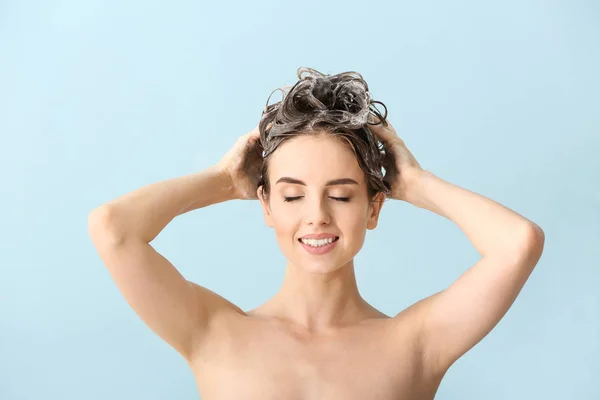 Beautiful young woman washing hair against color background — Stock Photo, Image