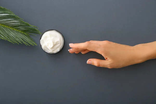 Female hand with natural cream on grey background