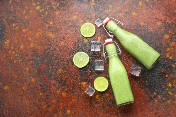 Bottles of fresh healthy smoothie, sliced citrus fruits and ice cubes on grunge background — Stock Photo, Image