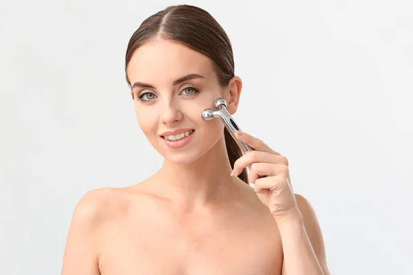 Mulher bonita com ferramenta de massagem facial no fundo branco — Fotografia de Stock