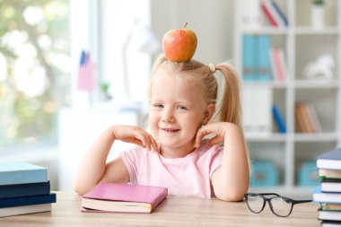 Sınıfta masada oturan elma ile Sevimli küçük kız öğrenci