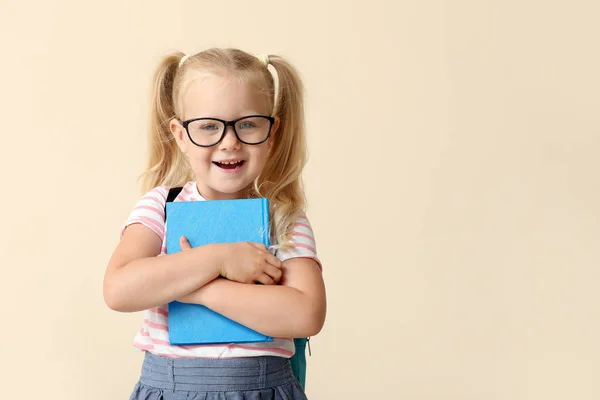Niedliches kleines Schulmädchen mit Buch auf hellem Hintergrund — Stockfoto