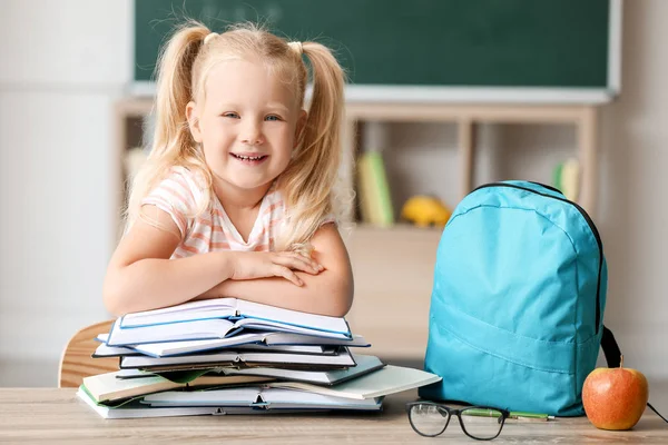 Schattige kleine schoolmeisje met boeken zittend op Bureau in klaslokaal — Stockfoto