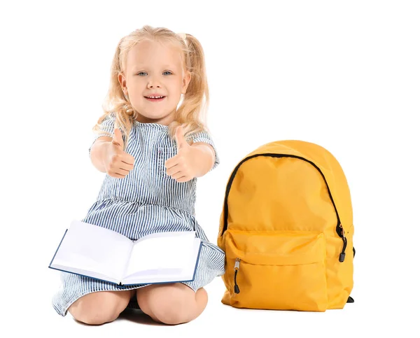 Aranyos kis iskolás a könyv és a hátizsák mutatja hüvelykujj-up fehér alapon — Stock Fotó