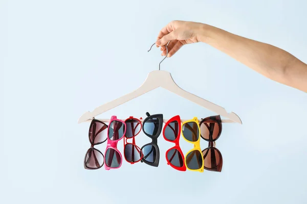 Vrouwelijke hand houden hanger met stijlvolle zonnebril op lichte achtergrond — Stockfoto