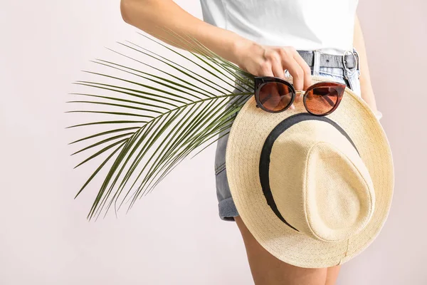 Jeune femme avec des lunettes de soleil élégantes, chapeau et feuille tropicale sur fond clair — Photo