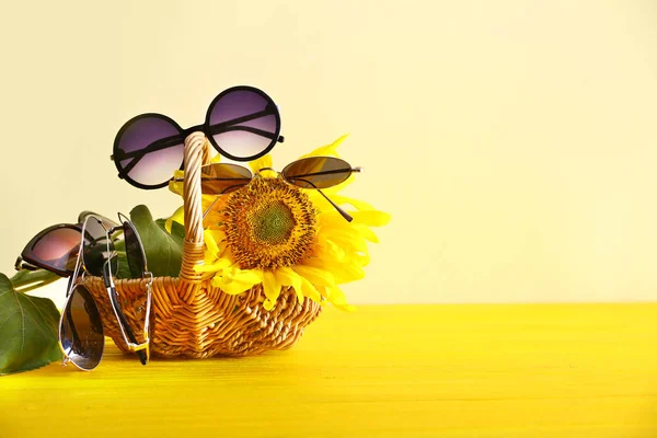 Stylish sunglasses with wicker basket and sunflower on color background — Stock Photo, Image