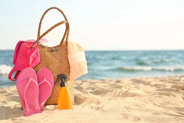 Bag with flip-flops, swimsuit, towel, sunglasses and cosmetics on sand beach — Stock Photo, Image
