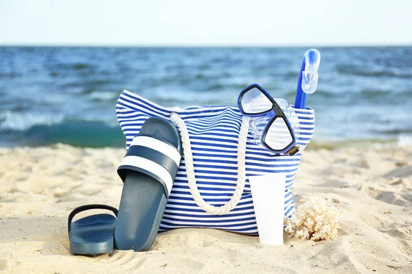 Bag with flip-flops, set or snorkeling and cosmetics on sand beach — Stock Photo, Image