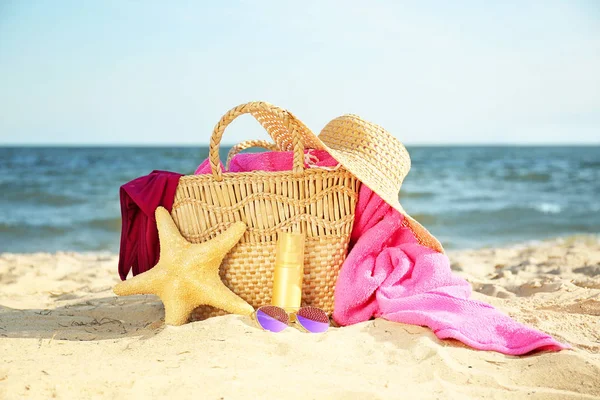 Bag with starfish, swimsuit, hat, sunglasses and cosmetics on sand beach