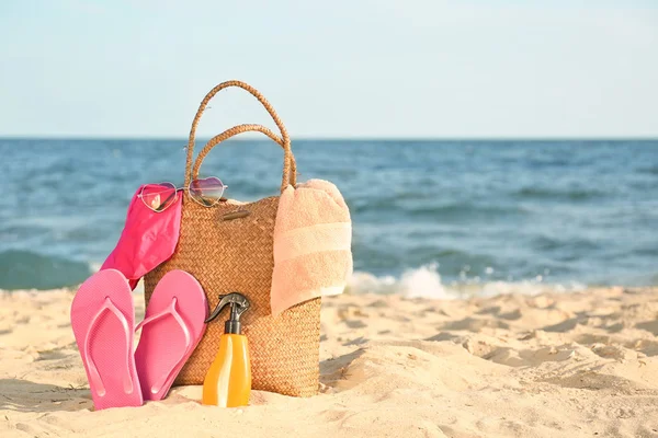 Bag with flip-flops, swimsuit, towel, sunglasses and cosmetics on sand beach — Stock Photo, Image