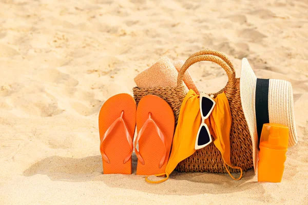 Bag with flip-flops, swimsuit, hat, sunglasses and cosmetics on sand beach — Stock Photo, Image