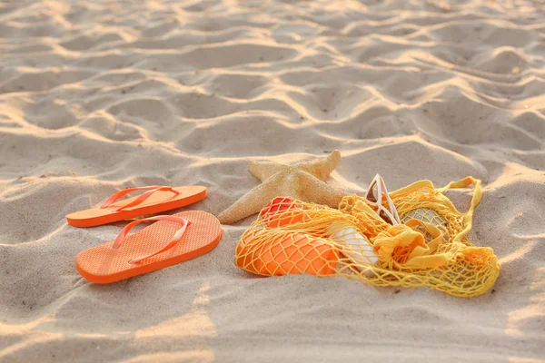 Flip-flops with mesh bag, sunglasses and cosmetics on sand beach — Stock Photo, Image