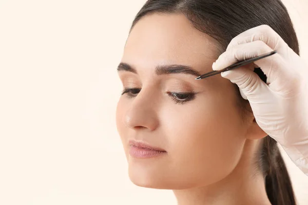 Ung kvinna genomgår ögonbrynskorrigering förfarande på ljus bakgrund — Stockfoto