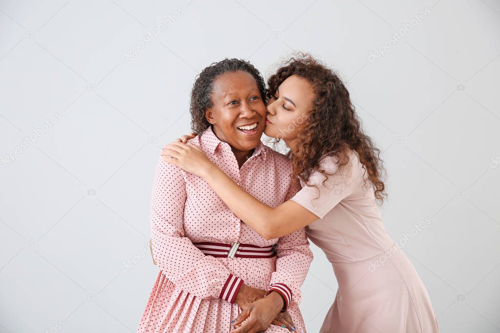 Portrait of African-American woman kissing her mother on light background