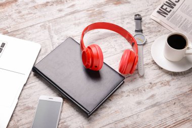 Modern kulaklıklar, dizüstü bilgisayar, dizüstü bilgisayar, bir fincan kahve ve açık ahşap arka plan üzerine gazete