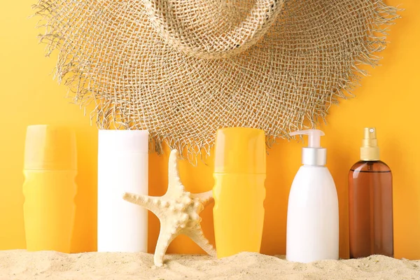 Different sun protection creams on sand against color background — Stock Photo, Image