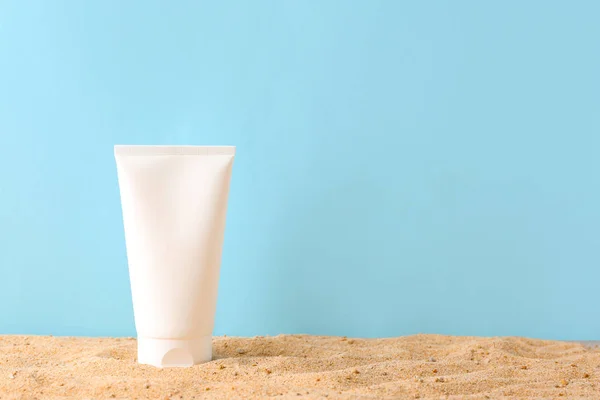 Tube of sun protection cream on sand against color background