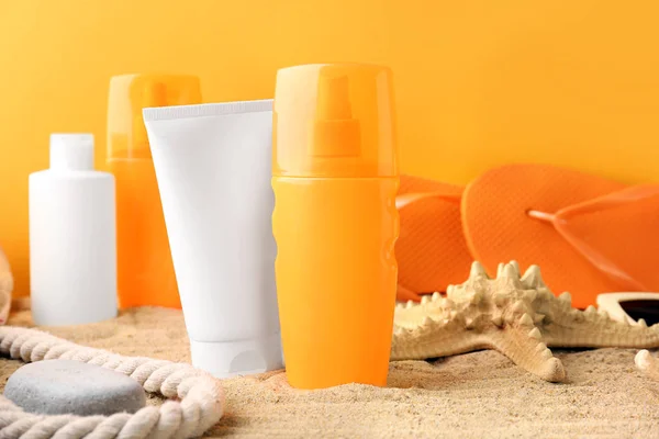 Different sun protection creams on sand against color background — Stock Photo, Image