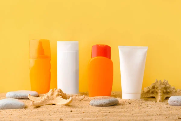 Different sun protection creams on sand against color background — Stock Photo, Image