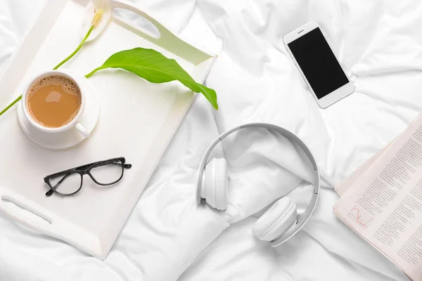 Modern headphones, cup of coffee, mobile phone and newspaper on bed — Stock Photo, Image