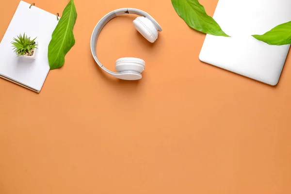 Modern headphones, laptop and notebook on color background
