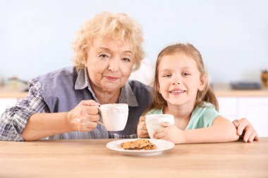 Sevimli küçük kız ve büyükanne mutfakta kurabiye ile çay içme