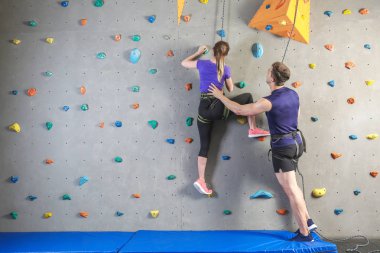 Genç kadına spor salonunda duvara tırmanmayı öğreten eğitmen